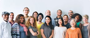 The image shows a diverse group of smiling team members gathered together in a bright office space, symbolizing collaboration, teamwork, and a positive work environment.